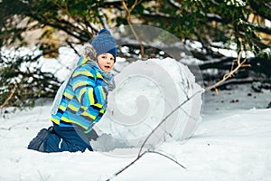 little cute boy making snowman. rolling big snowball