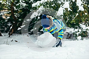 little cute boy making snowman. rolling big snowball