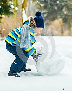 little cute boy making snowman. rolling big snowball