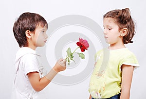 A little cute boy is offering a rose to little gir