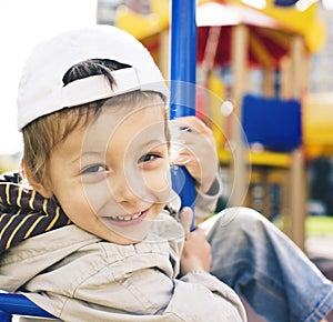 Little cute boy playing on playground, hanging on a gymnastic ring smiling