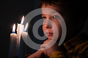 Little cute boy praying in front of a burning candle
