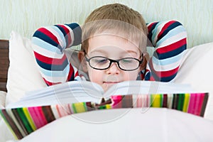 Little cute boy reading book in bed