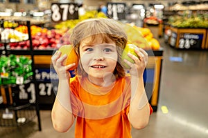 Little cute boy with shopping cart full of fresh organic vegetables and fruits standing in grocery department of food