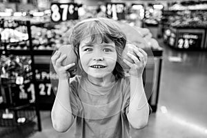 Little cute boy with shopping cart full of fresh organic vegetables and fruits standing in grocery department of food