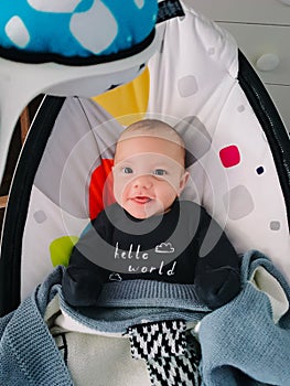 Little cute boy sitting in baby rocker and smiling. Modern toys and center for children.