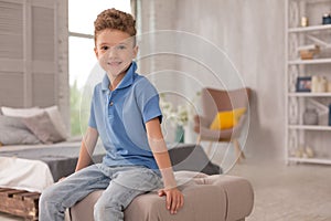 Little cute boy sitting on hassock in living room