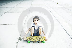 Little cute boy with skateboard on playground alone training, making funy faces