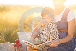 Little cute boy son and his beautiful pregnant mom at picnic