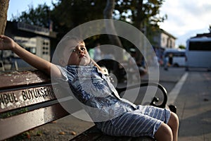 little cute caucasian boy sits on a bench and makes faces.