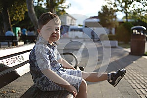 little cute caucasian boy sits on a bench and makes faces.