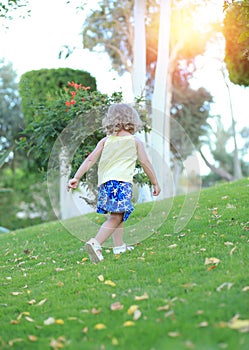 Little cute Caucasian girl with curls in a yellow T-shirt walks at sunset in a green park. Childhood. Nature beautiful