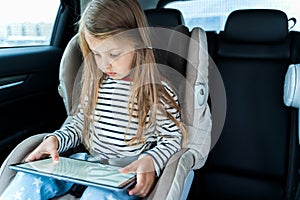 Little cute caucasian girl is driving in car. Online school learning,education.Playing video games in tablet. Traveling on road in