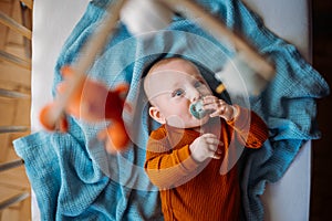 Little cute causian baby boy with pacifier, boy looks at the toy and is delighted.