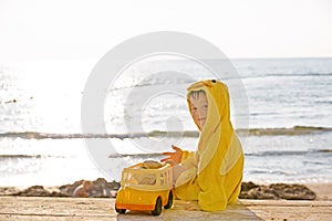 Little cute child baby boy sitting at sea on sand beach, play with toy car truck. Little kid son playing outdoors. Love