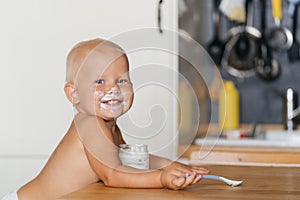 Little cute child experiences happiness and joy, eats yogurt with a spoon soiling