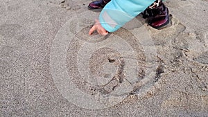 Little cute child girl drawing smile face in beach sand, family love concept