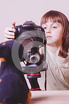 Little cute child girl photographer takes portrait of toy dog with a DSLR camera