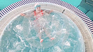 Little cute child girl in swimsuit, swim cap and goggles having a rest in swimming pool