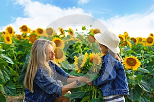 Little cute child giving her mother sunflowers on field with sunflowers.