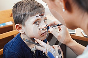 Little cute child making facepaint on birthday party, zombie Apocalypse facepainting, halloween preparing concept