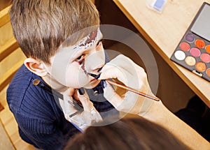 Little cute child making facepaint on birthday party, zombie Apocalypse facepainting, halloween preparing concept