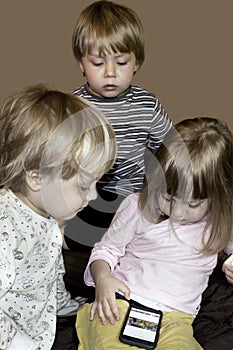 Little cute curious blonde triplets watch cartoons on smartphone photo