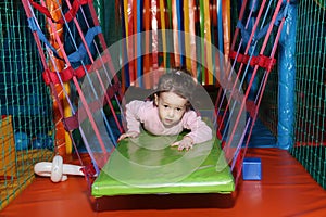 Little cute curly baby girl playing in a children`s entertainment center in the game maze. The child plays in the playground