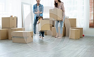 Little cute daughter helping mother and father to move big cardboard box while father clap his hands to cheer up.