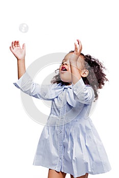 Little cute fashionable african american girl in blue dress catches soap bubbles on white background