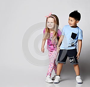 Little cute frolic kids Asian boy and blonde girl play hide and seek together, stand holding hands looking at copy space