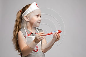 Little cute funny girl playing wearing doctor uniform holding toy syringe looking at camera