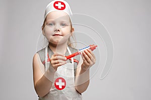 Little cute funny girl playing wearing doctor uniform holding toy syringe looking at camera