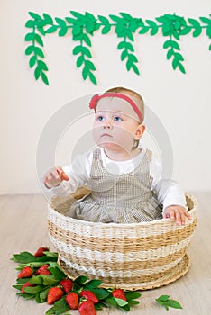 Little cute girl 1 year old in a wicker basket decorated with red juicy strawberries. Healthy eating