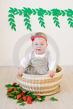 Little cute girl 1 year old in a wicker basket decorated with red juicy strawberries. Healthy eating