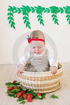 Little cute girl 1 year old in a wicker basket decorated with red juicy strawberries. Healthy eating