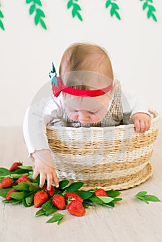 Little cute girl 1 year old in a wicker basket decorated with red juicy strawberries. Healthy eating