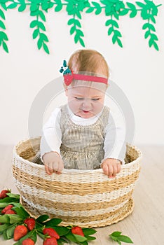 Little cute girl 1 year old in a wicker basket decorated with red juicy strawberries. Healthy eating