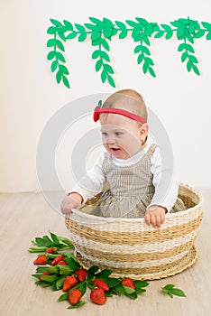 Little cute girl 1 year old in a wicker basket decorated with red juicy strawberries. Healthy eating