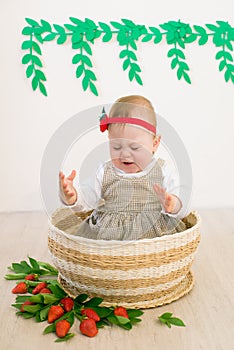 Little cute girl 1 year old in a wicker basket decorated with red juicy strawberries. Healthy eating