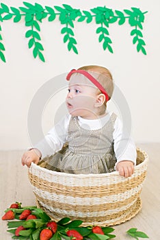 Little cute girl 1 year old in a wicker basket decorated with red juicy strawberries. Healthy eating