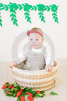 Little cute girl 1 year old in a wicker basket decorated with red juicy strawberries. Healthy eating