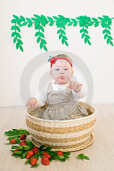 Little cute girl 1 year old in a wicker basket decorated with red juicy strawberries. Healthy eating