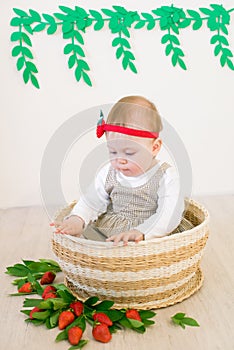 Little cute girl 1 year old in a wicker basket decorated with red juicy strawberries. Healthy eating