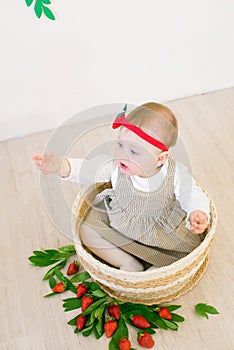 Little cute girl 1 year old in a wicker basket decorated with red juicy strawberries. Healthy eating