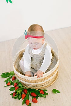 Little cute girl 1 year old in a wicker basket decorated with red juicy strawberries. Healthy eating