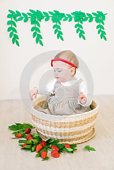 Little cute girl 1 year old in a wicker basket decorated with red juicy strawberries. Healthy eating