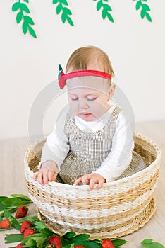 Little cute girl 1 year old in a wicker basket decorated with red juicy strawberries. Healthy eating