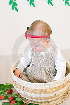 Little cute girl 1 year old in a wicker basket decorated with red juicy strawberries. Healthy eating