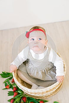 Little cute girl 1 year old in a wicker basket decorated with red juicy strawberries. Healthy eating